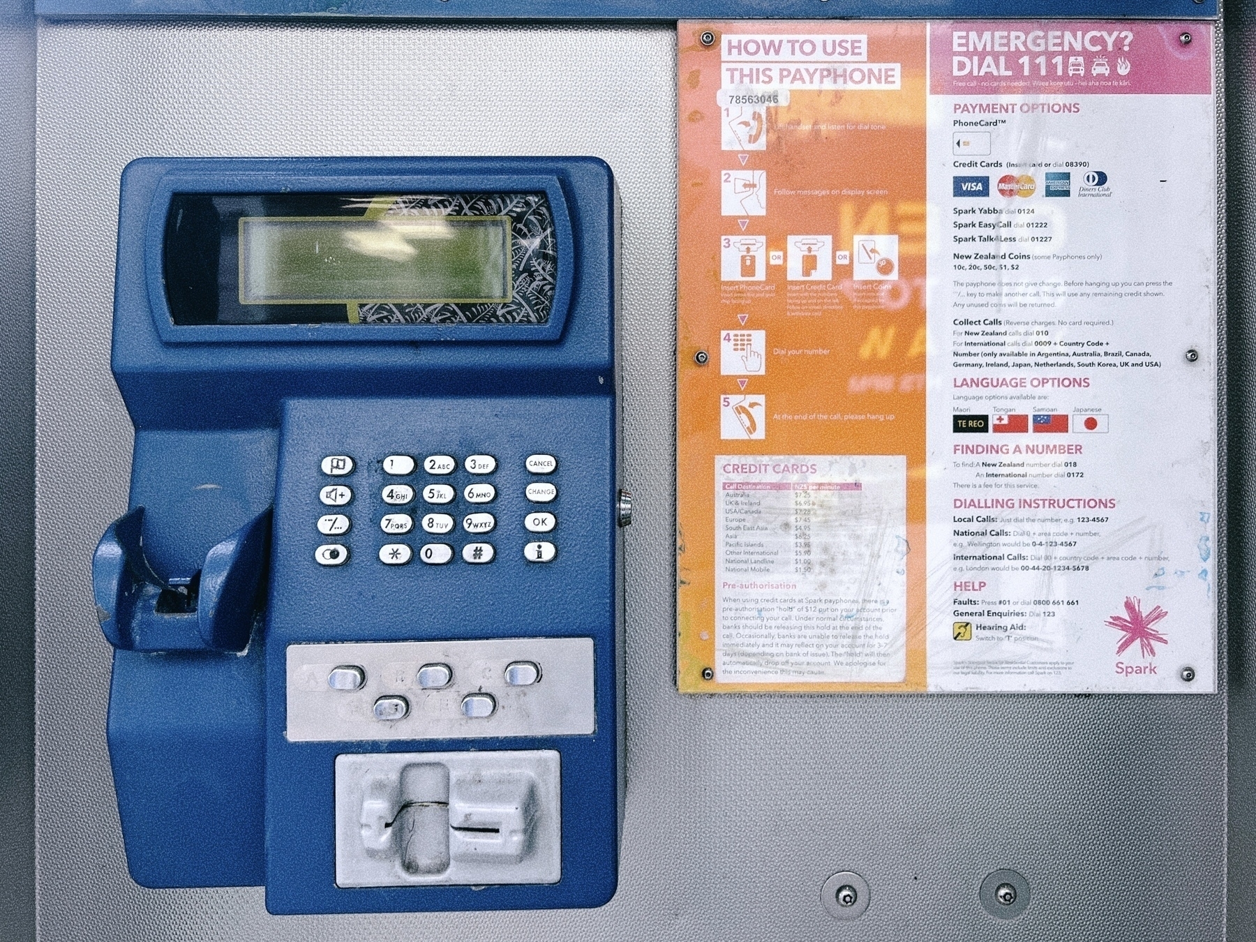 A public payphone featuring a keypad and coin slot is shown alongside an instructions panel with emergency contact information and payment options. Unfortunately the payphone lacks a handset, or power. 