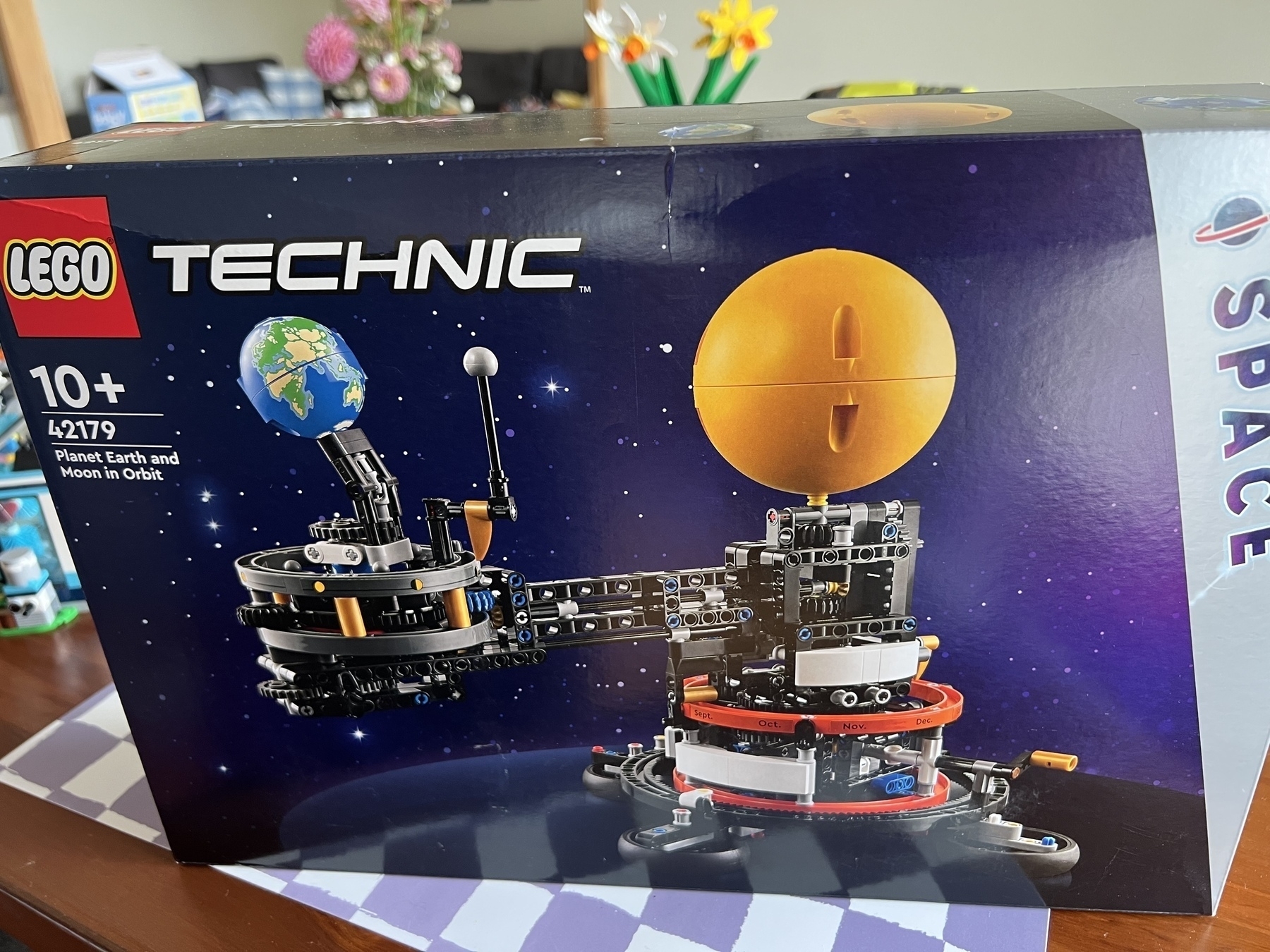 A LEGO Technic box featuring a set designed to build a model of the planets Earth and Moon in orbit is shown on a table.