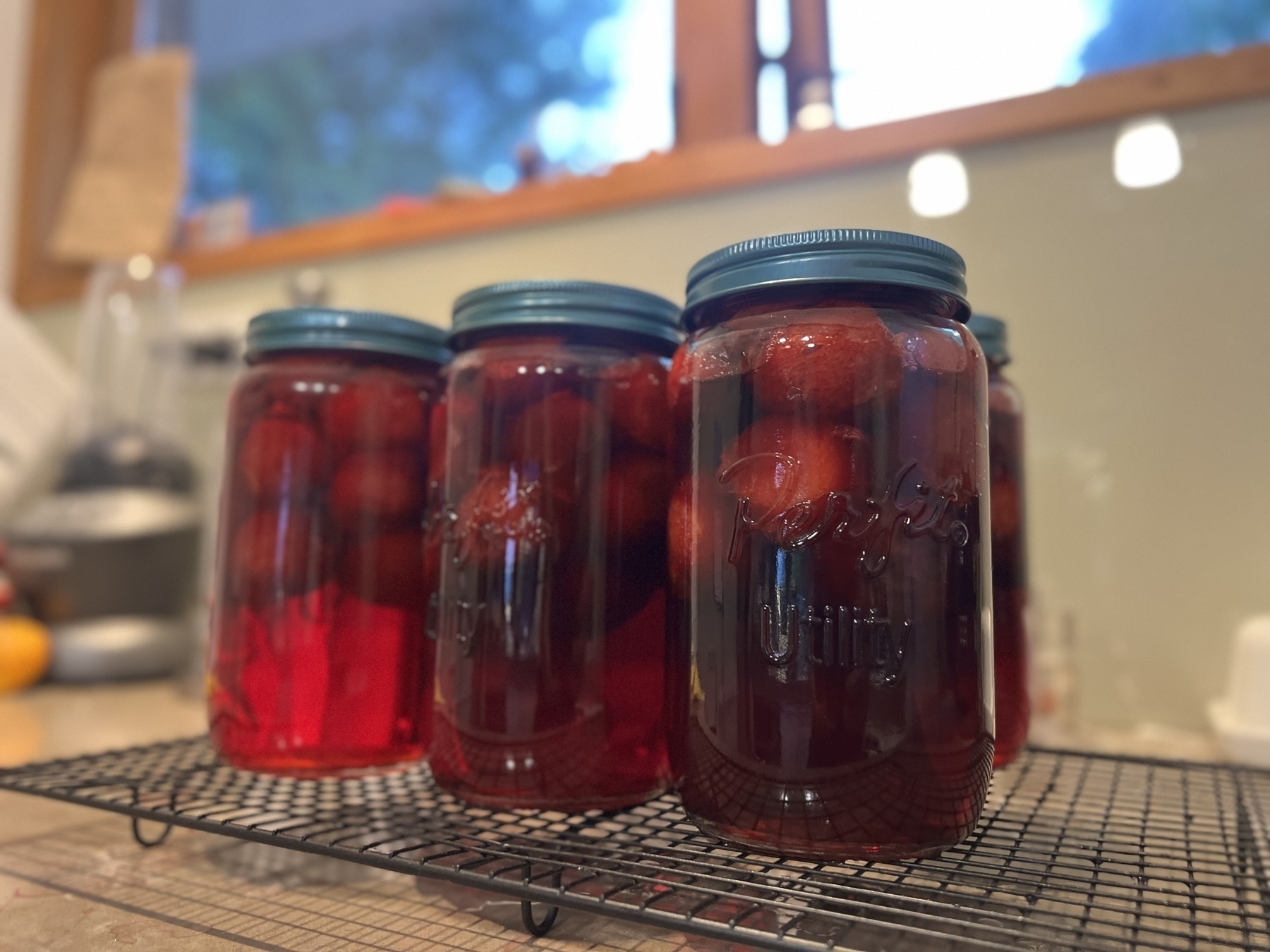 Several jars of preserved red fruits are cooling on a wire rack in a kitchen setting.