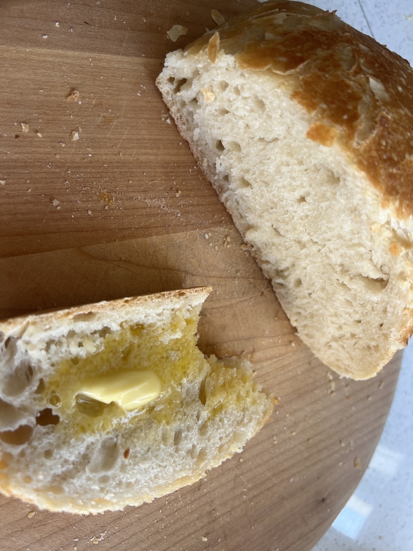 Two slices of rustic bread, one with a pat of butter, are placed on a wooden cutting board.